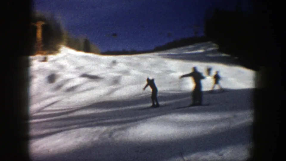 Several distant skiers gather or pass on an Aspen ski slope, silhouetted against sunlit snow in 1961 8mm footage.