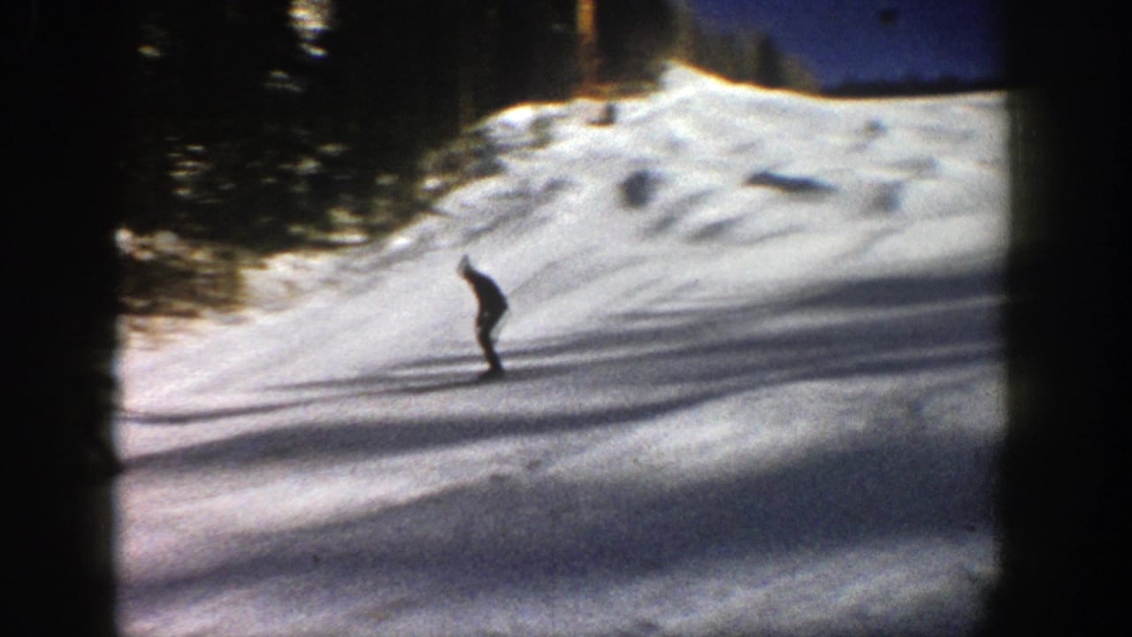 A distant skier moves across a sunlit snowy slope in 1961 Aspen, Colorado, with evergreens behind the run.
