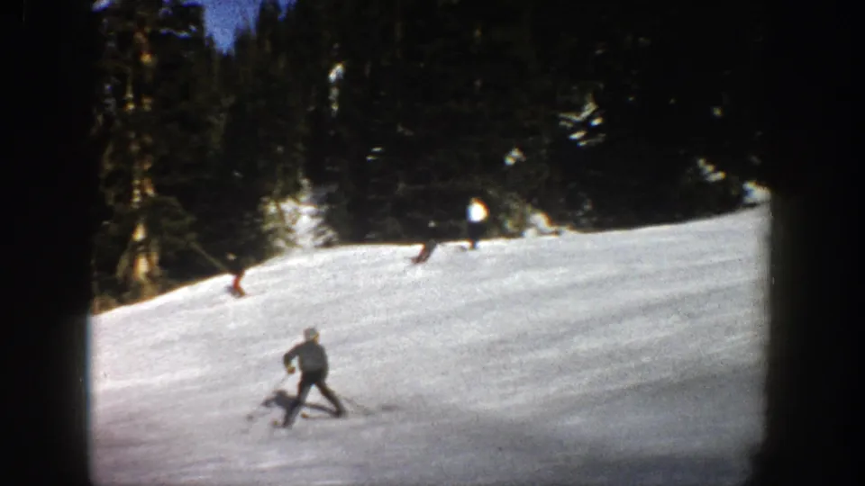 A skier in dark winter clothing moves across the lower slope in Aspen, with another skier near the trees in the background.