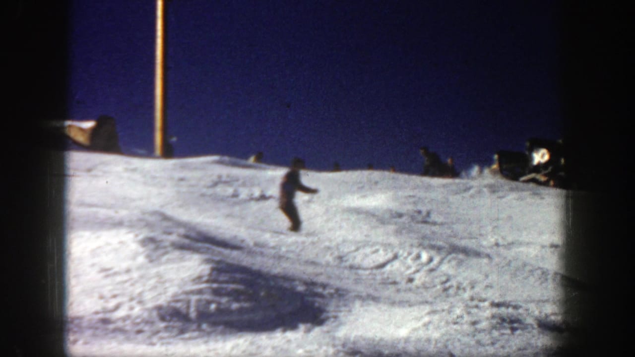 A distant skier crosses a snow-covered Aspen slope in 1961 home-movie footage, framed by dark 8mm film edges.