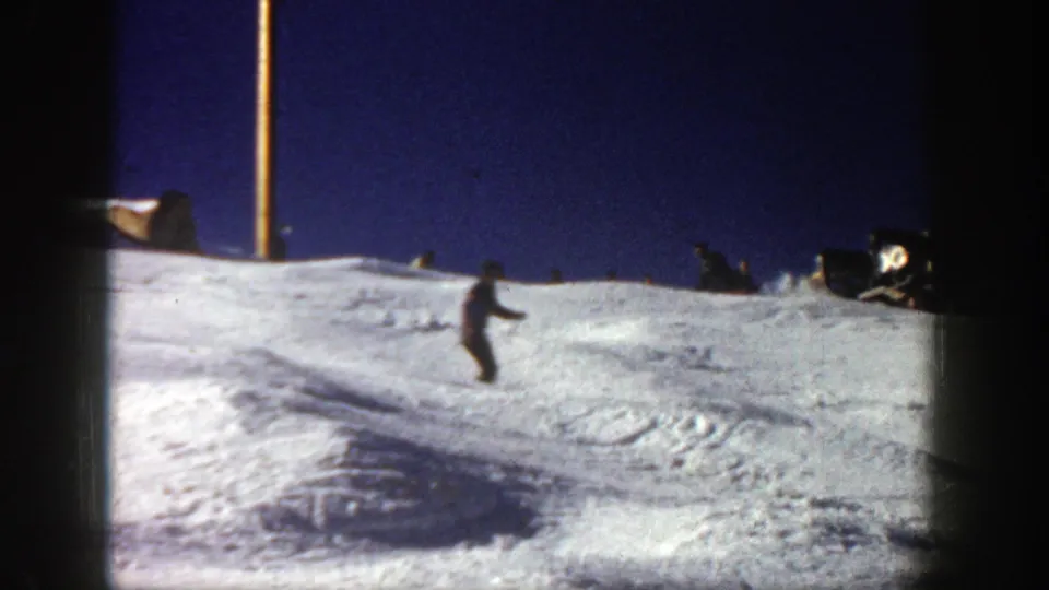 A distant skier crosses a snow-covered Aspen slope in 1961 home-movie footage, framed by dark 8mm film edges.