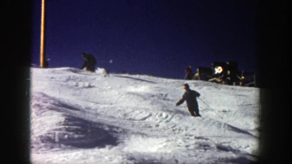 A skier in dark winter clothing turns on an Aspen snow slope, with 8mm frame edges and ridge objects visible.