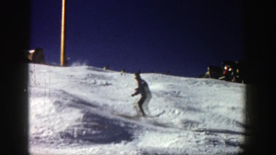 A distant skier continues downhill on a sunlit Aspen slope, with grain, gate edges, and snow shadows visible.