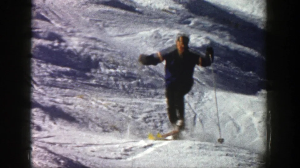 A close 1961 Aspen frame shows a skier facing the camera while descending over bright, uneven snow.