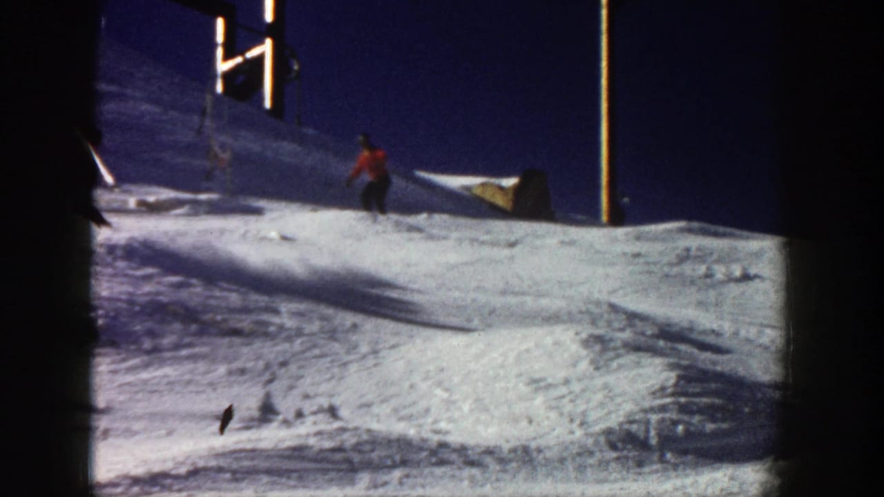 Skier in a red jacket descending a snowy slope beside ski lift poles.