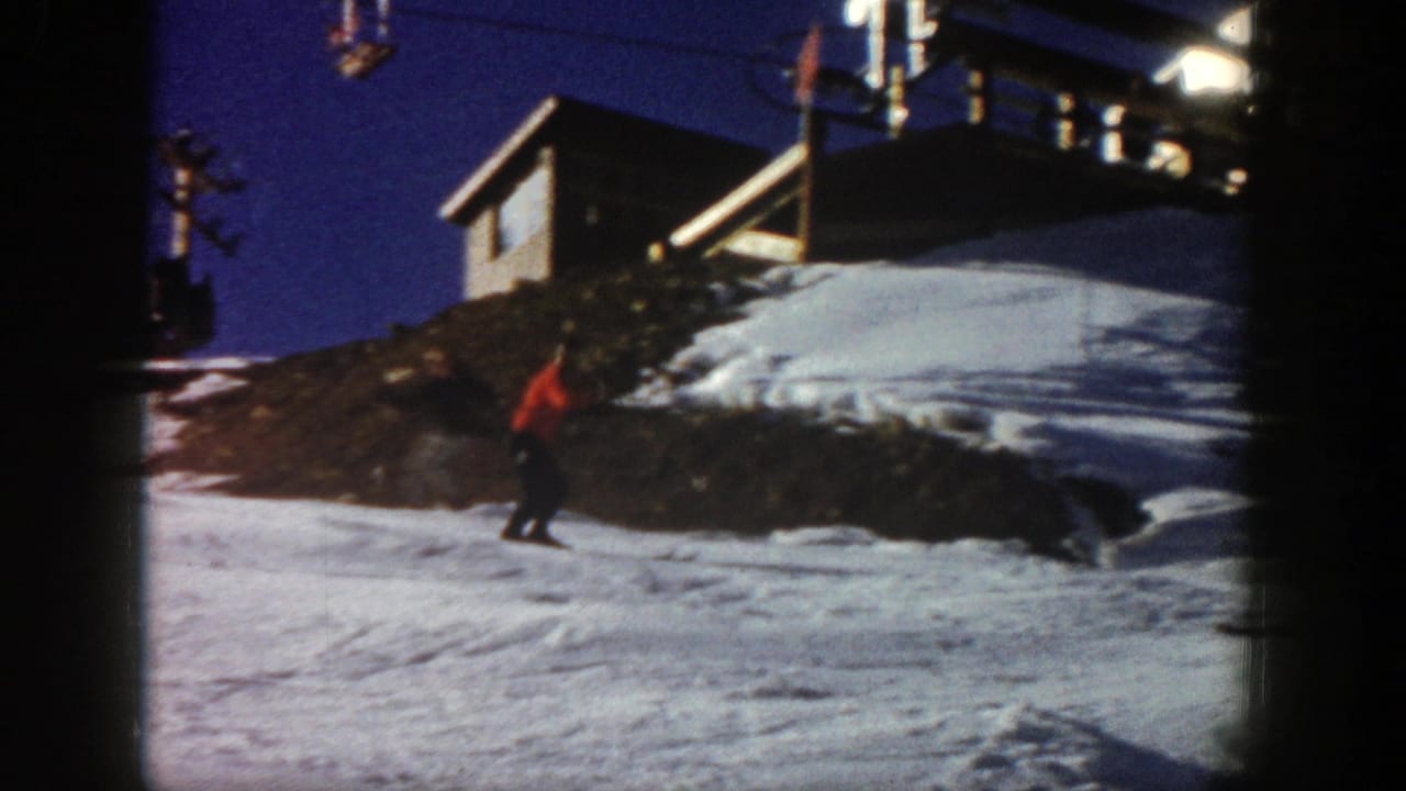 Skier in red moving across a snow-covered slope below a lift structure.