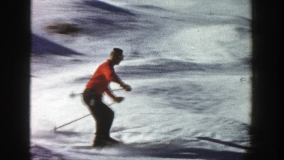 Near the end of the 1961 Aspen clip, the skier crouches slightly while continuing downhill across textured snow.