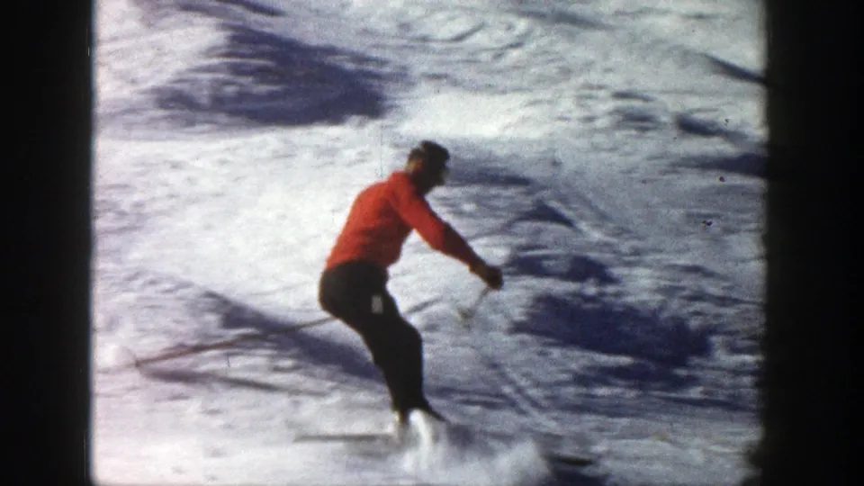 Adult skier in a red jacket makes a downhill turn on a snowy Aspen slope in 1961 home-movie footage.
