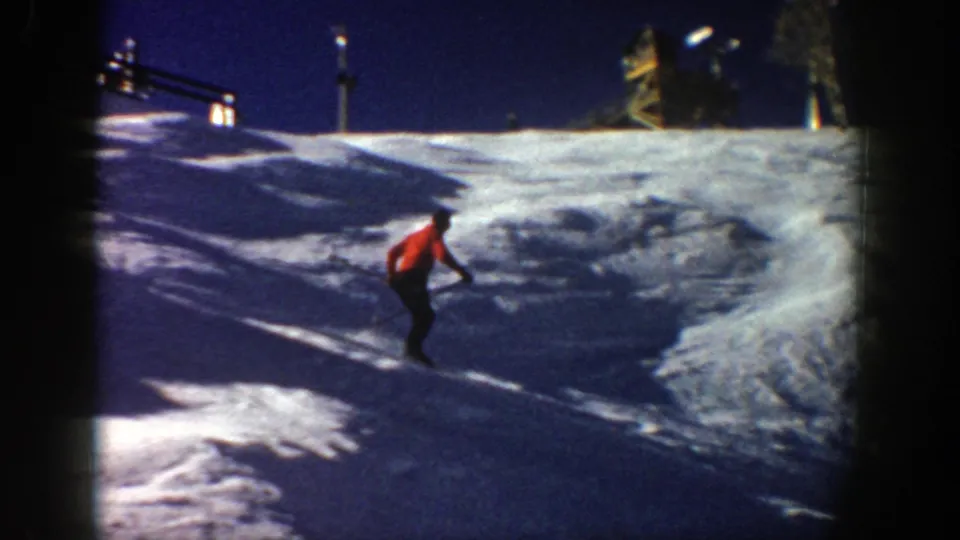 The skier continues downhill beneath a ridge, with a ski lift structure visible in the Aspen winter setting.
