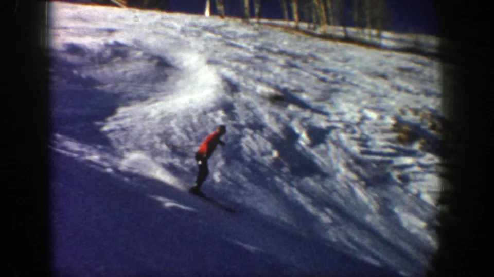 A distant skier in red crosses a wide, tracked snow slope in the 1961 Aspen 8mm footage.