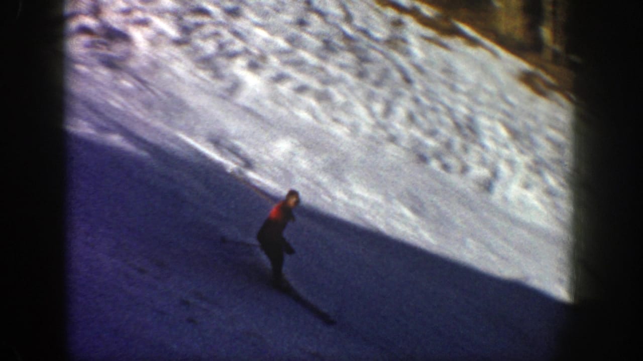 Skier in a red jacket descends a shadowed snowy slope.