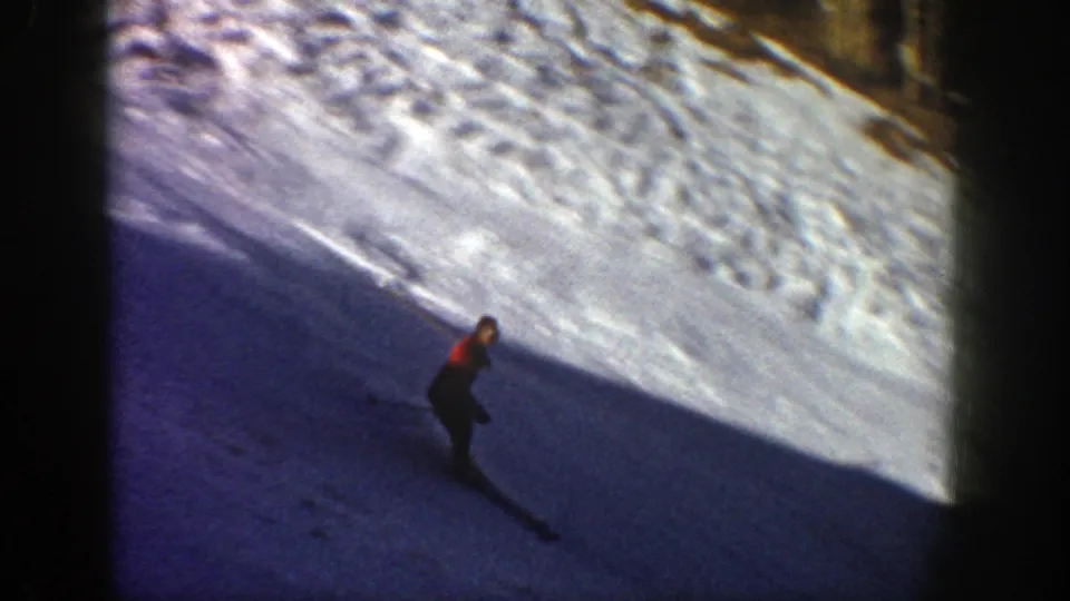 In 1961 Aspen, Colorado 8mm footage, a skier in a red jacket moves downhill across a snowy slope with strong sun and shadow.