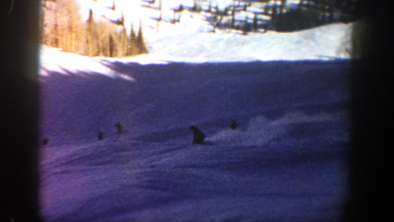 Distant riders on a snowy slope with trees and dark film borders.