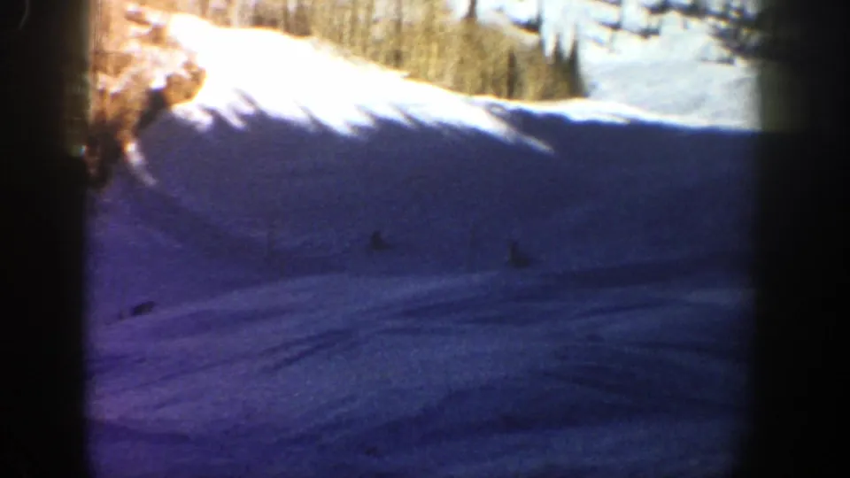 Distant figures cross a blue-tinted snow slope in Aspen, with bright snow and trees visible near the top of the frame.