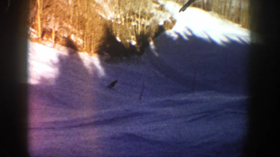 A small rider silhouette descends a snowy Aspen hill, framed by trees, shadows, and rounded 8mm film edges.