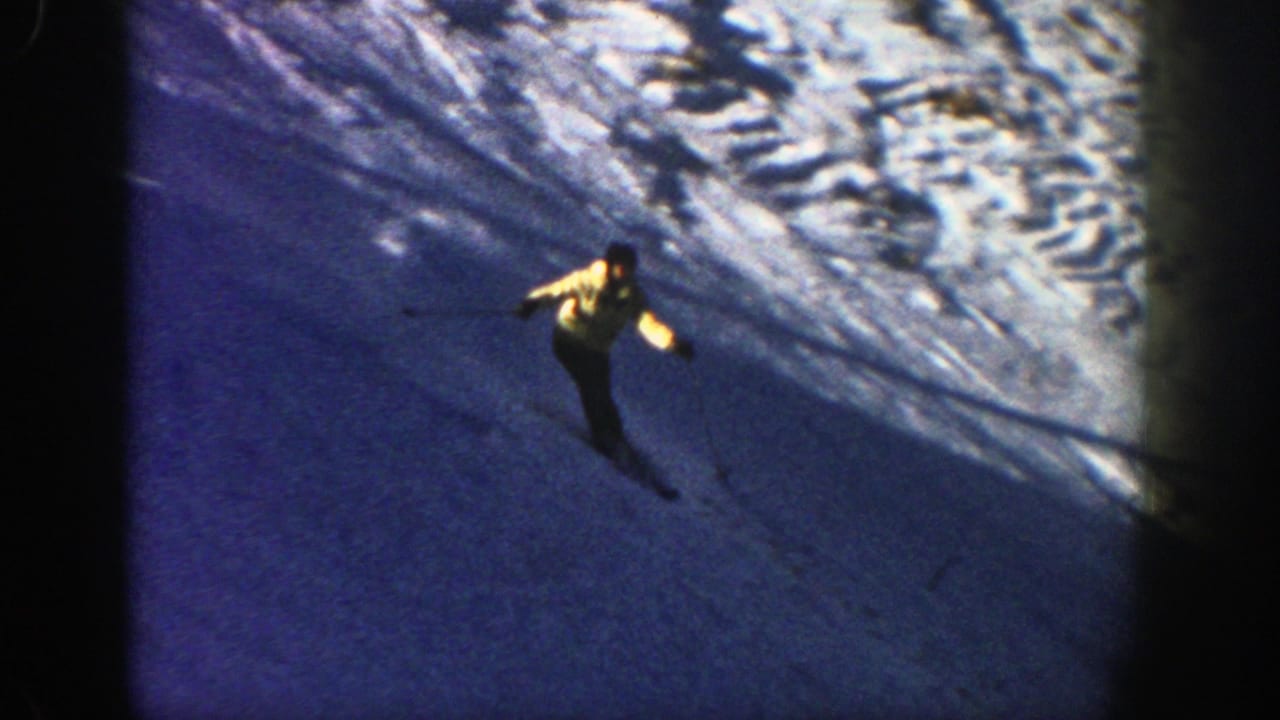 A skier in 1961 Aspen footage descends a snowy slope with poles, framed by dark 8mm borders and blue winter shadows.