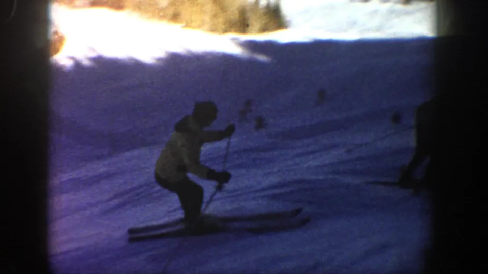 A skier appears close to the camera on a blue-shadowed Aspen ski slope, with another dark figure partly visible nearby.