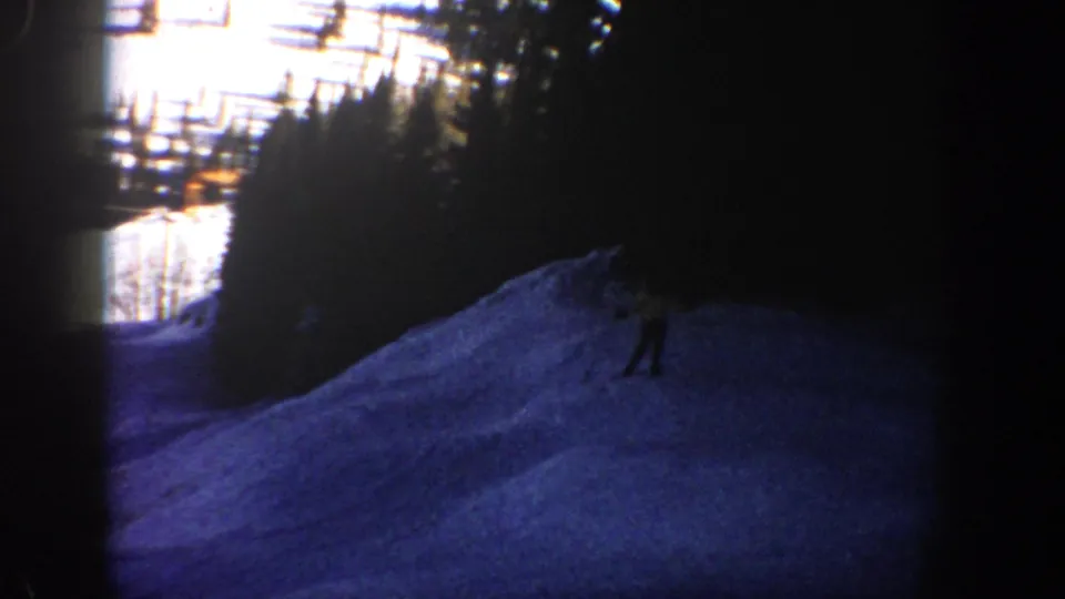 Near the end of the 1961 Aspen clip, a skier appears small against the blue-tinted snow and dark tree line.