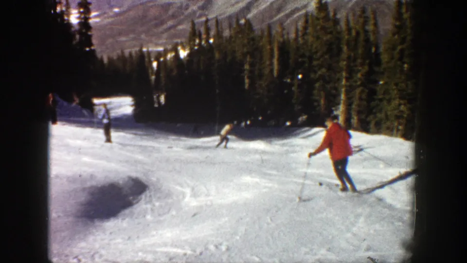 1961 Aspen frame with a red-jacketed skier in the foreground and other skiers descending a sunny mountain run.