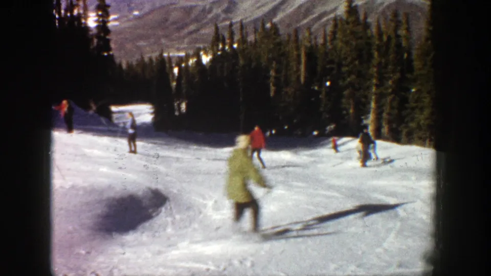 1961 Aspen ski footage frame with a light-coated skier moving close to camera and other skiers farther up the snowy slope.