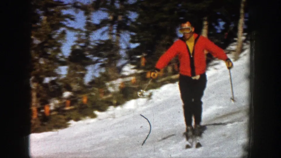 The red-jacketed skier comes closer on the Aspen slope, with trees and another distant person behind him.