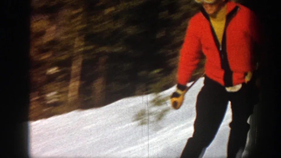 Cropped close view of the skier in red and dark pants passing the handheld camera on the snowy Aspen slope.
