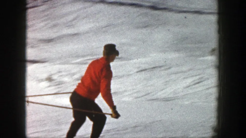 The adult skier in a red jacket and dark pants cuts across the Aspen snow, seen in soft 8mm color with poles extended.