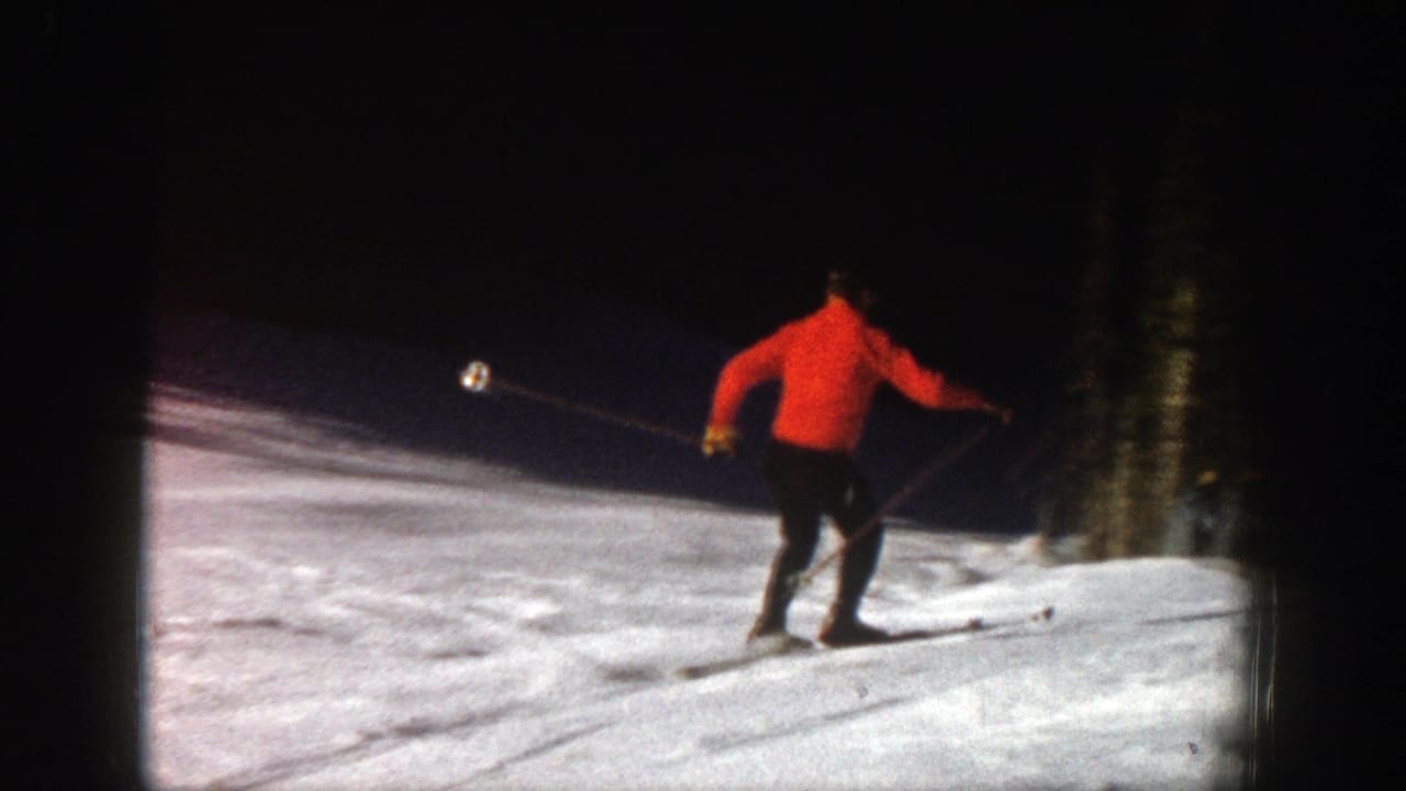 Skier in a red sweater moves across a snowy slope near dark evergreen trees.