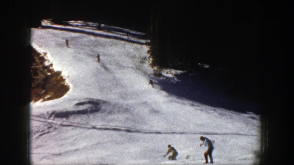 1961 Aspen ski scene with multiple people positioned across a sunlit, icy slope in grainy 8mm footage.