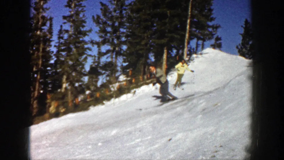 Two adults ski downhill on a snow-covered slope in Aspen, Colorado, in 1961 home-movie footage.