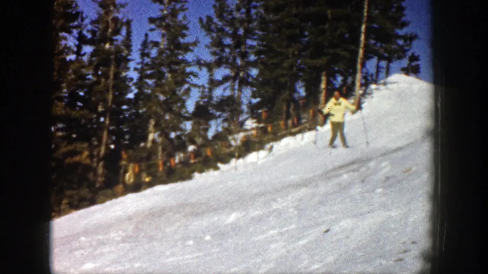 An adult skier moves across a wooded Aspen snow slope in 1961 archival home-movie footage.