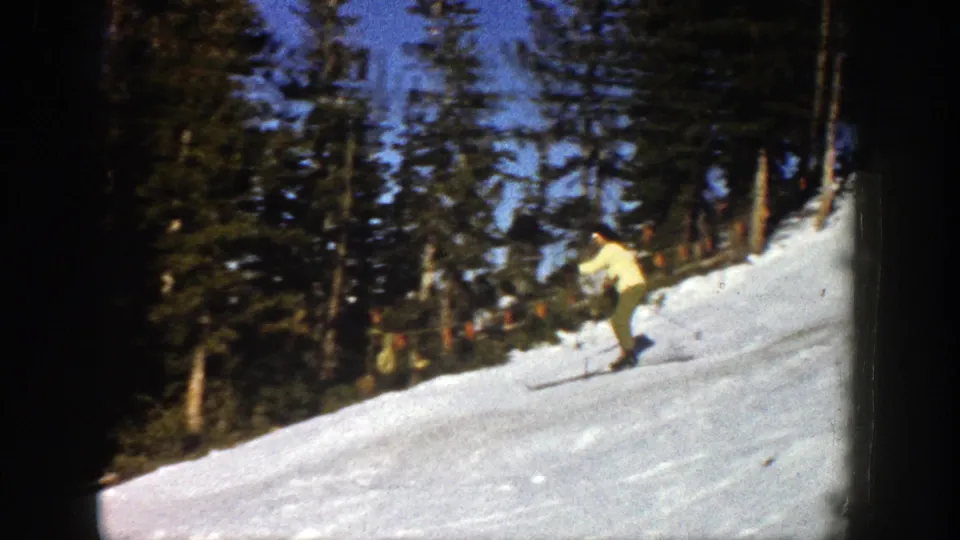 Two adult skiers continue downhill on a sunlit Aspen slope in 1961 8mm footage.