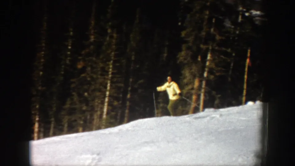 The skier comes closer on the snowy Aspen slope, using poles while evergreen trees form a dark background in the 8mm frame.