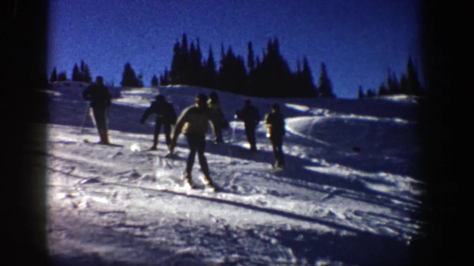 1961 Aspen frame with a small group of skiers on a bright snowfield under a deep blue sky.