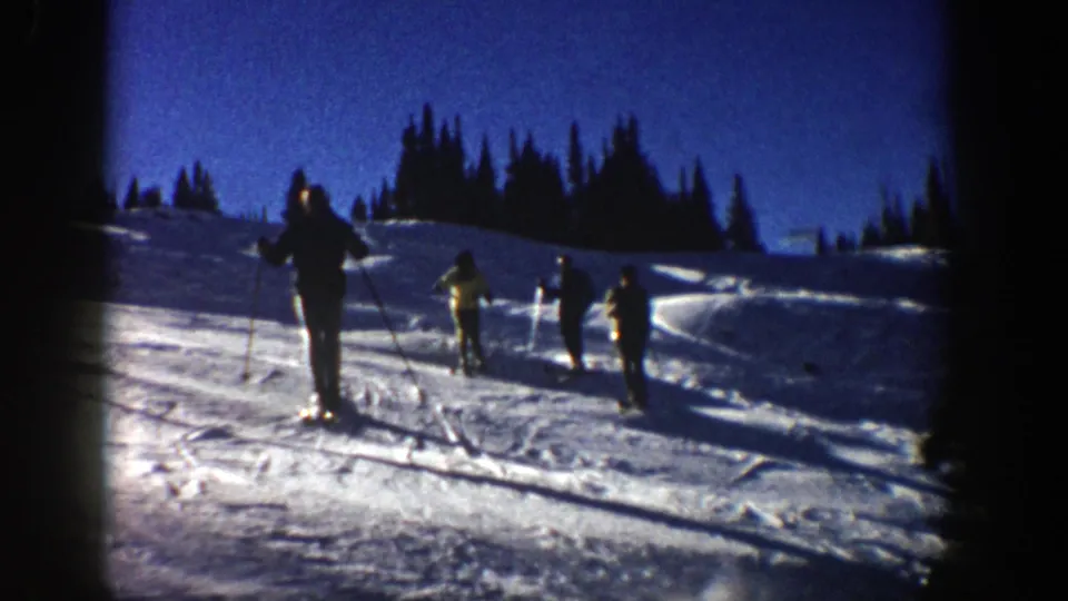 In metadata-supported 1961 Aspen, several skiers descend a snowy slope under a deep blue sky with pine trees behind them.