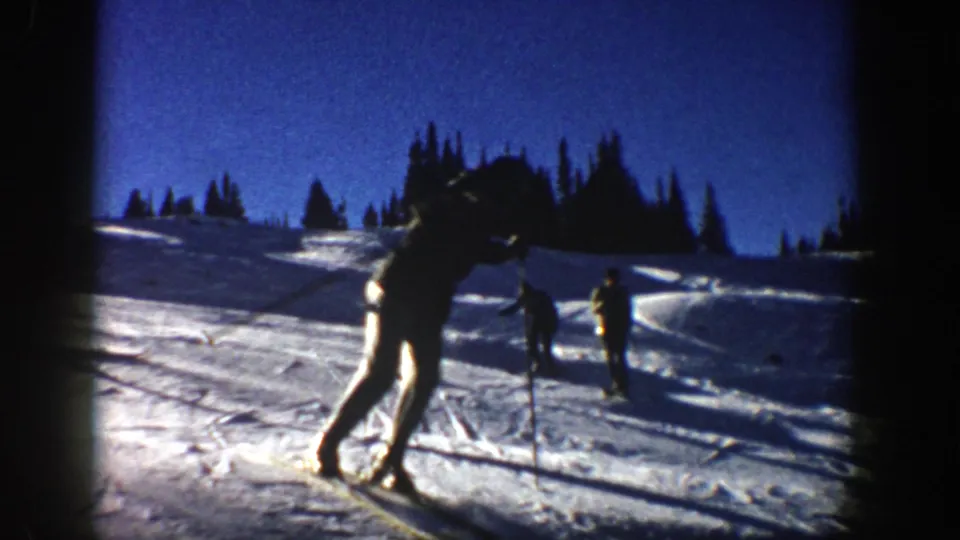 A skier in the foreground leans into motion on an Aspen snow slope, with other skiers spread across the hill behind.