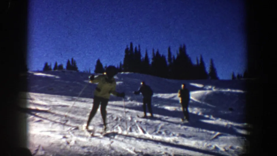 A light-jacketed skier moves near the camera on the snowy Aspen hill while two darker figures ski farther back.