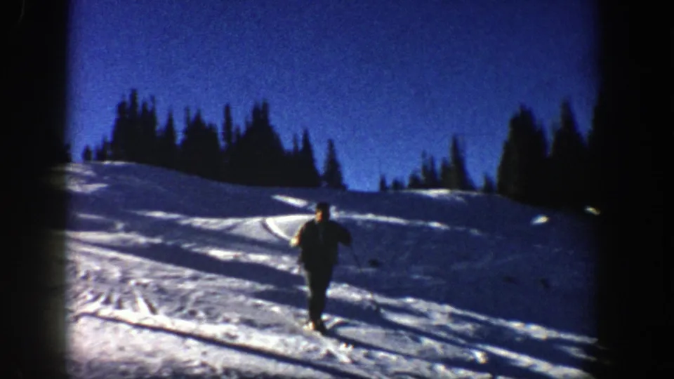 An adult skier travels away from the camera on an open Aspen snow slope, framed by dark trees and high-contrast 8mm color exposure.