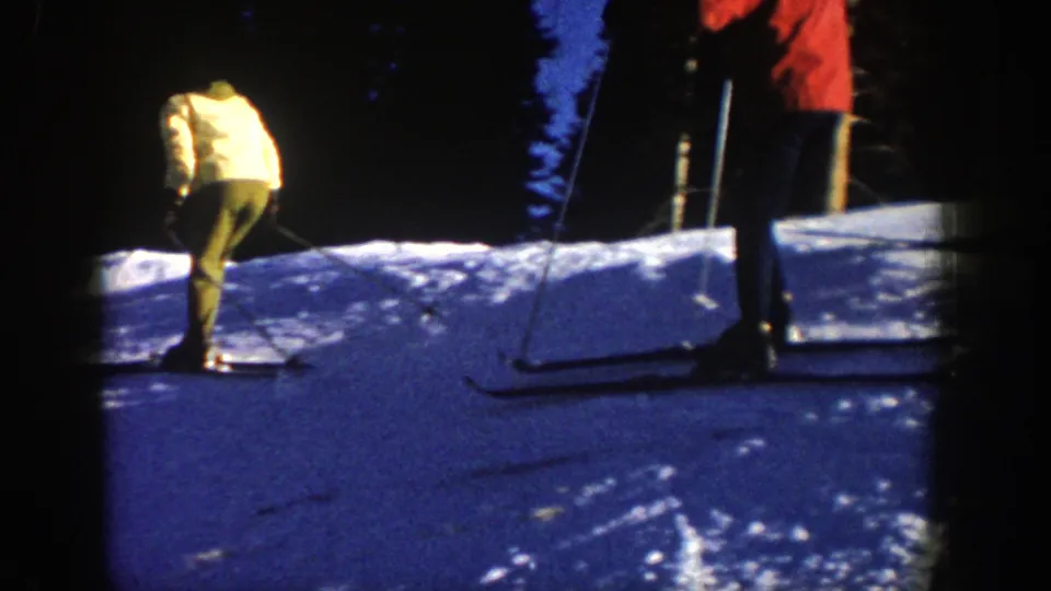 1961 Aspen frame with a skier in a yellow jacket standing on skis near a bright snowy slope edge.