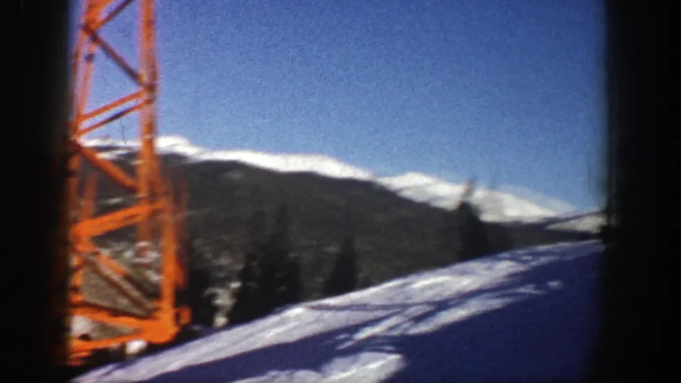 1961 Aspen frame showing a red metal tower structure beside snowy terrain and distant mountain ridges.