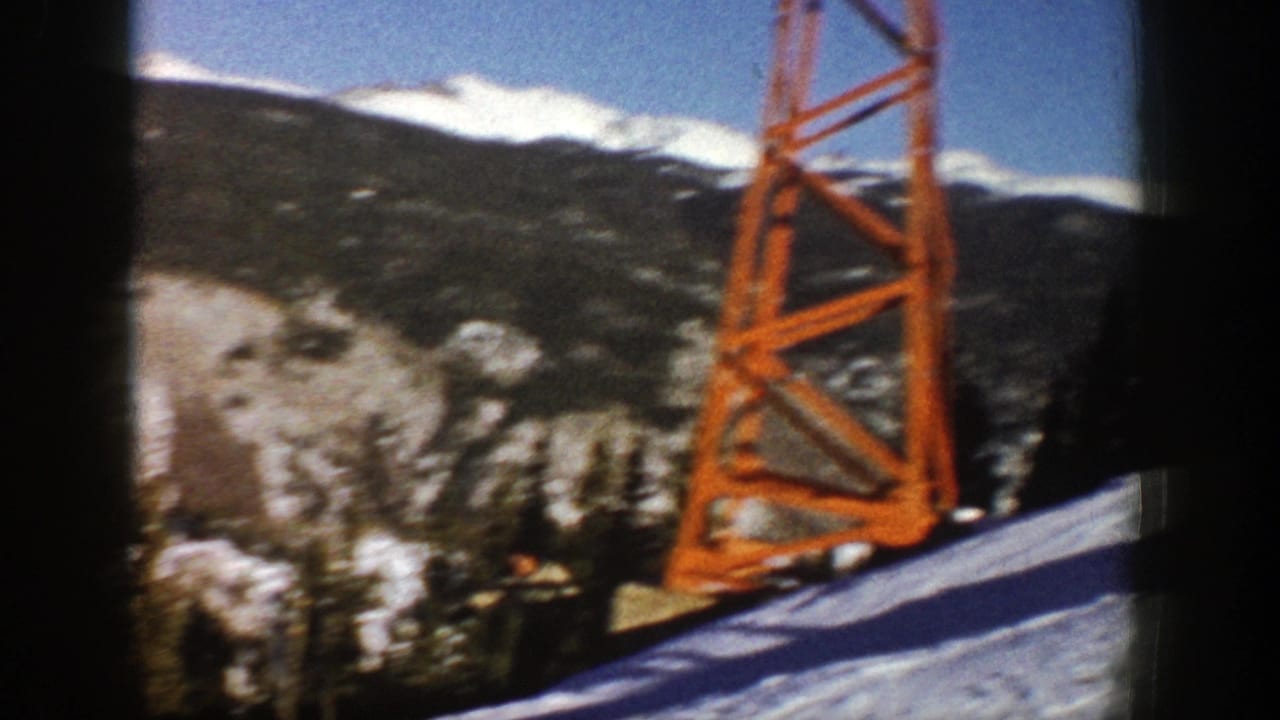 Orange ski lift tower beside snowy slope with mountains and trees in the background.