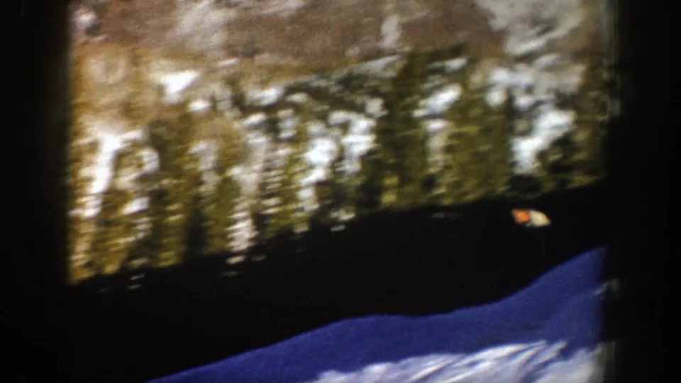 Handheld 8mm frame of an Aspen ski slope, with blue-shadowed snow, a dark treeline, and rocky winter mountain terrain beyond.