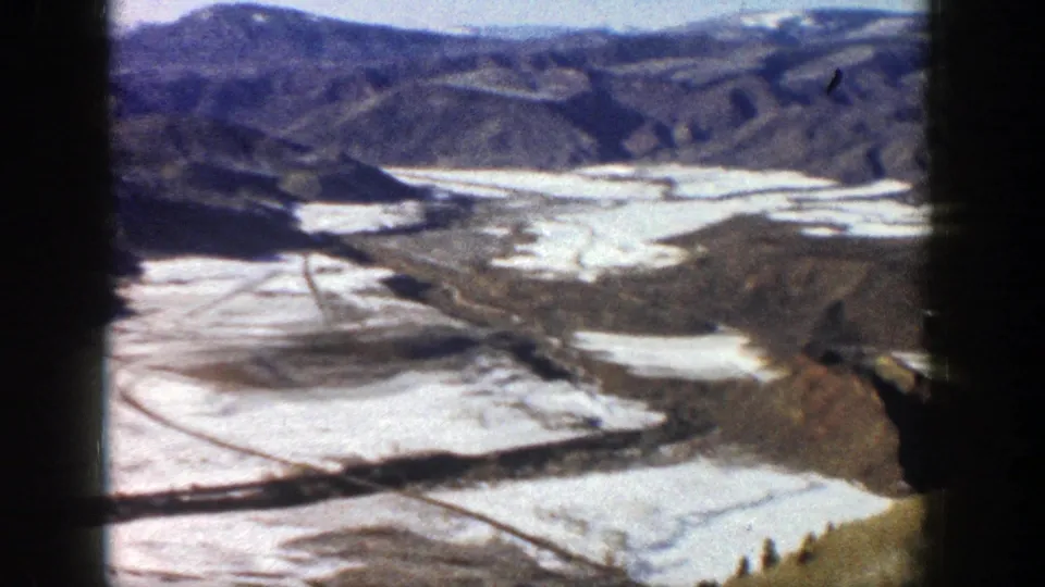 1961 Aspen, Colorado 8mm aerial view of a broad valley with melting snow fields, brown slopes, and distant mountain ridges.