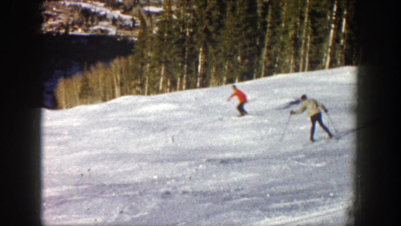 Two skiers on an Aspen, Colorado snow slope in 1961, one in a red jacket and one in a light jacket, framed by dark 8mm borders.