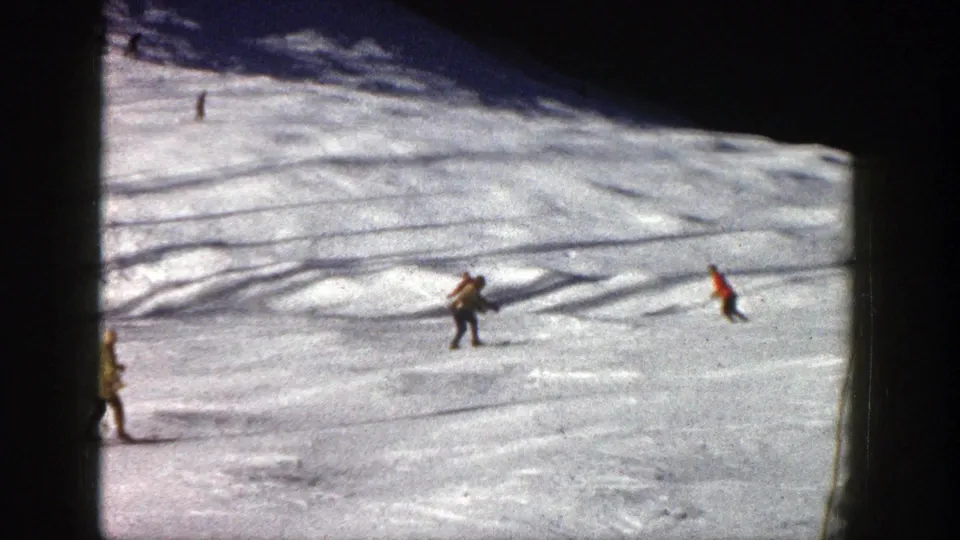 A dark-clothed skier and a red-jacketed skier move over the Aspen snow, with the 8mm frame edge visible.