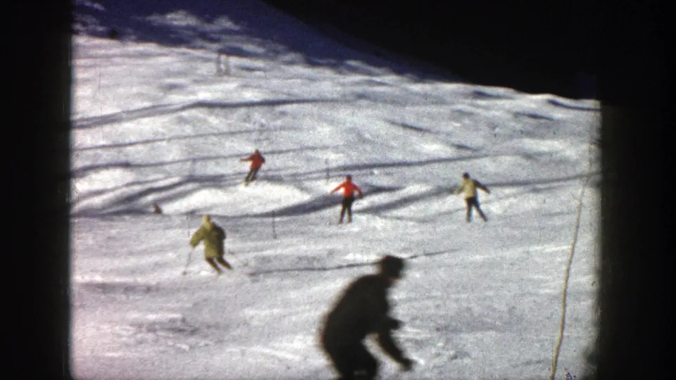 Four skiers are visible on the Aspen slope, including a foreground figure blurred by motion and distance in the 8mm frame.
