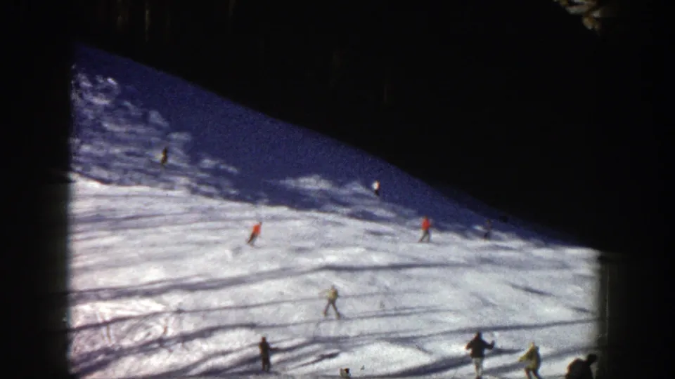 1961 Aspen ski-slope view with scattered skiers in bright coats moving across sunlit snow and shadowed terrain.