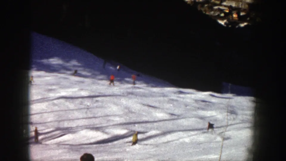 Wide 1961 Aspen ski scene showing skiers spaced across a snowy run with long shadows and visible 8mm frame borders.