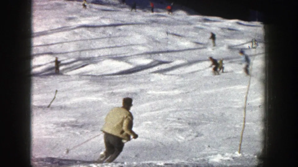 Close foreground skier on a 1961 Aspen slope with several background skiers moving across sunlit snow.