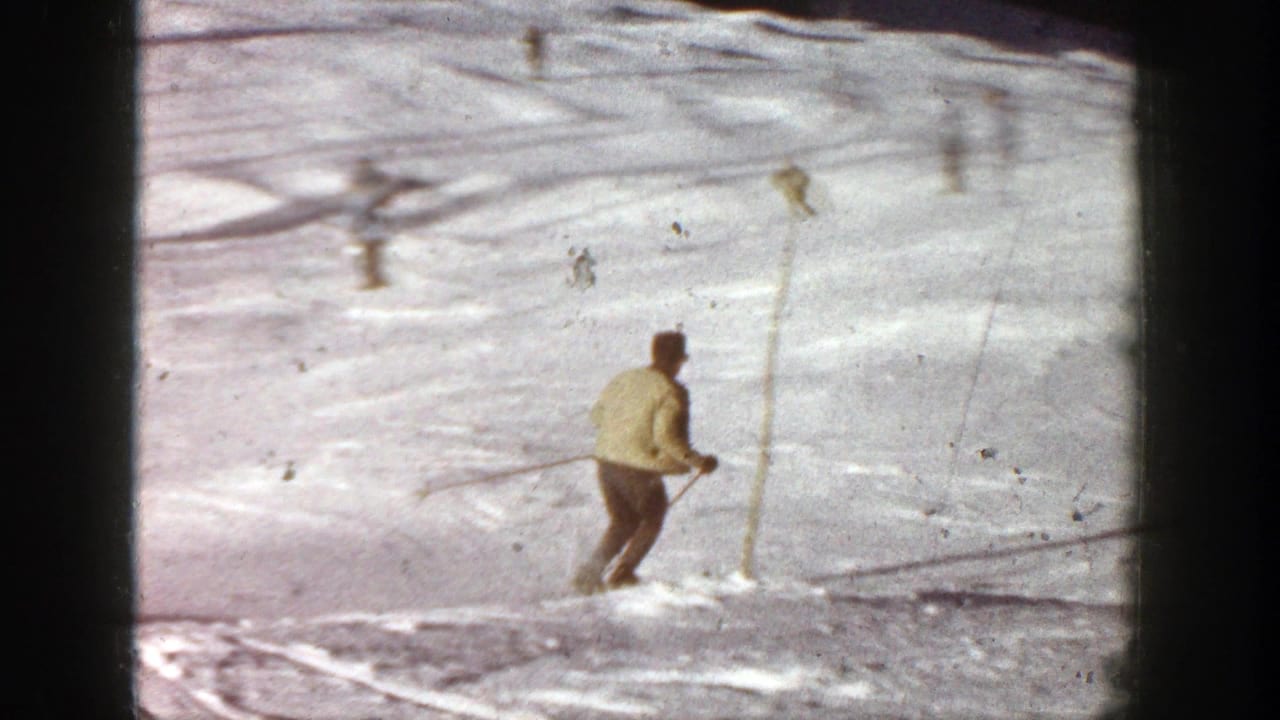 Skier in a pale yellow jacket descends a snowy slope with poles.